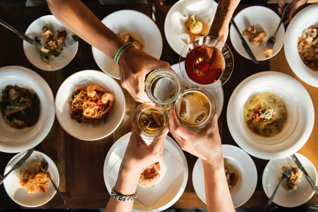 Friends clinking glasses over a table filled with pasta and gourmet dishes.