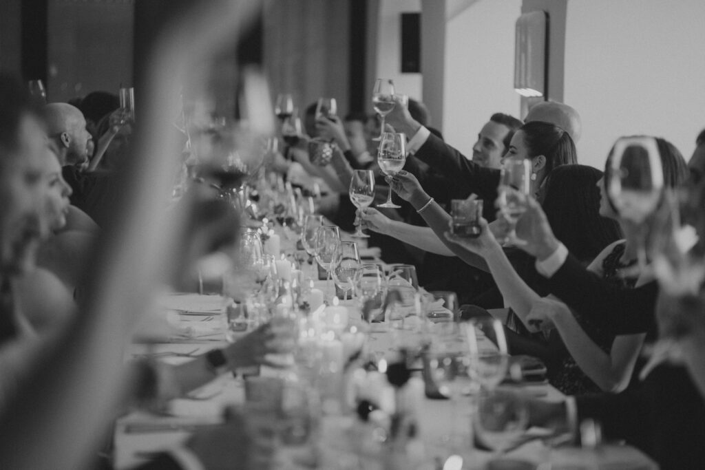 A black and white photo of a long table of people in formal attire raising their glasses for a toast.